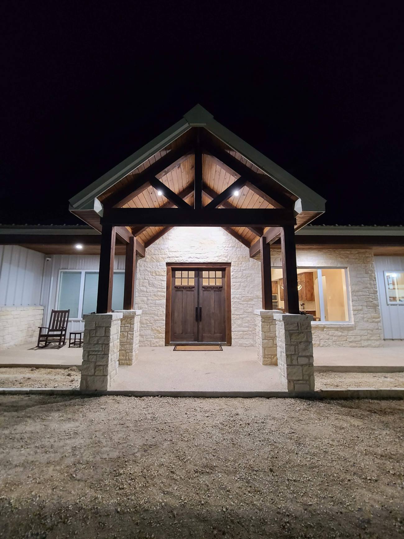 Custom stone-and-timber home, lit entry at night — I Am Home Innovations, Conroe TX